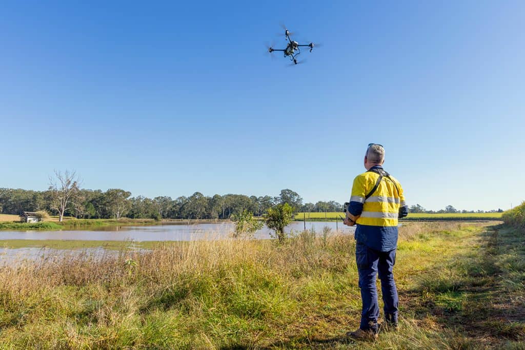 Drone flying over rural farmland near water bodies, showcasing innovative farming technology at Templeton Farming Enterprises.